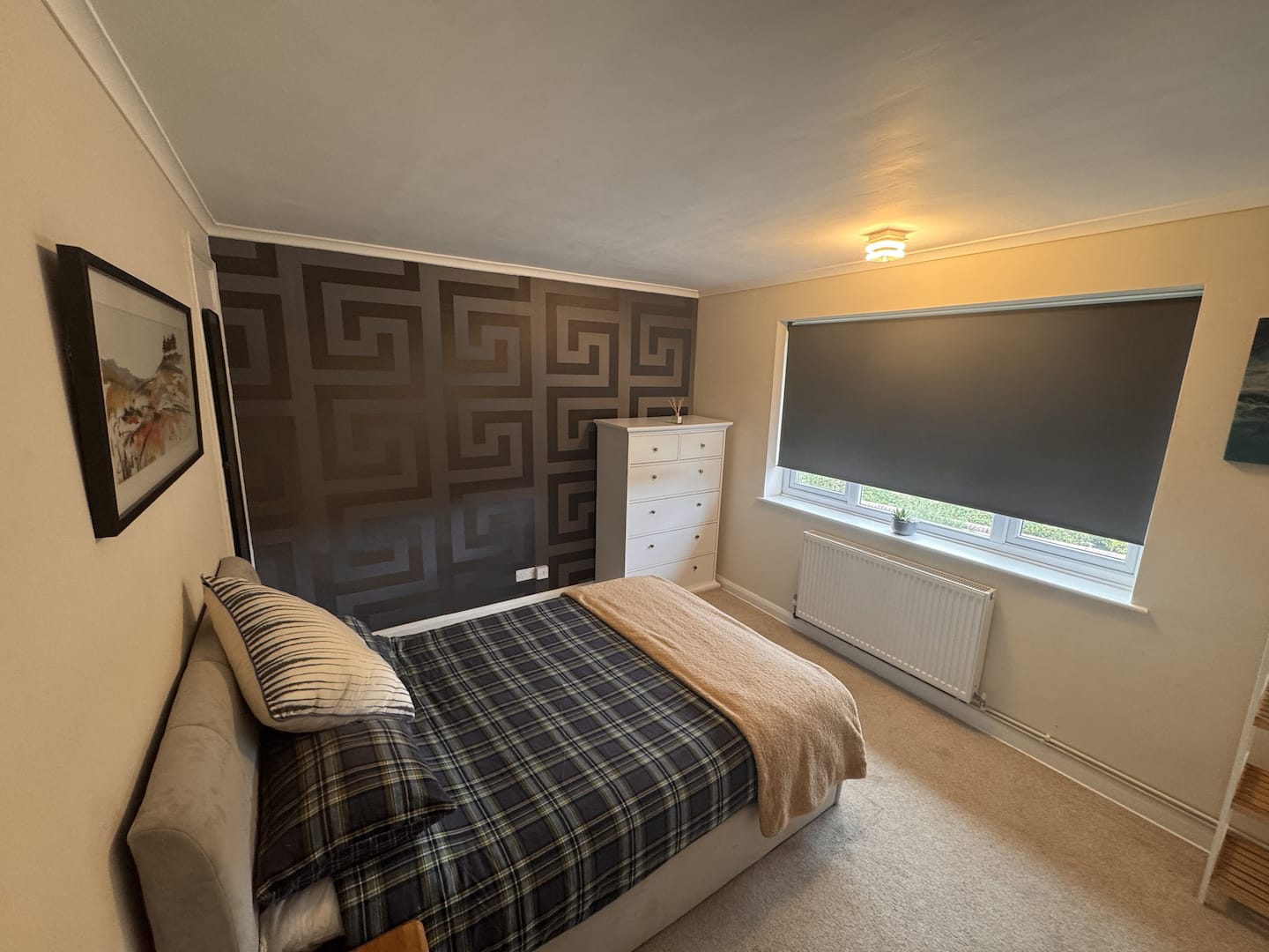 Double bedroom with checked bedding, a large window and a patterned feature wall